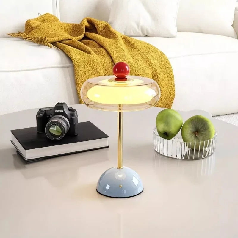 Blue Sorrel glass lamp on a white table beside a camera