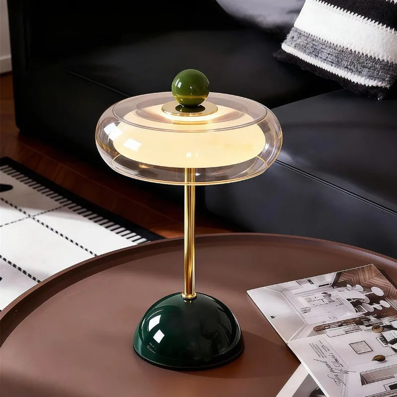 Dark green Oria rechargeable glass table lamp on a wood side table beside a leather sofa