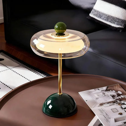 Dark green Oria rechargeable glass table lamp on a wood side table beside a leather sofa
