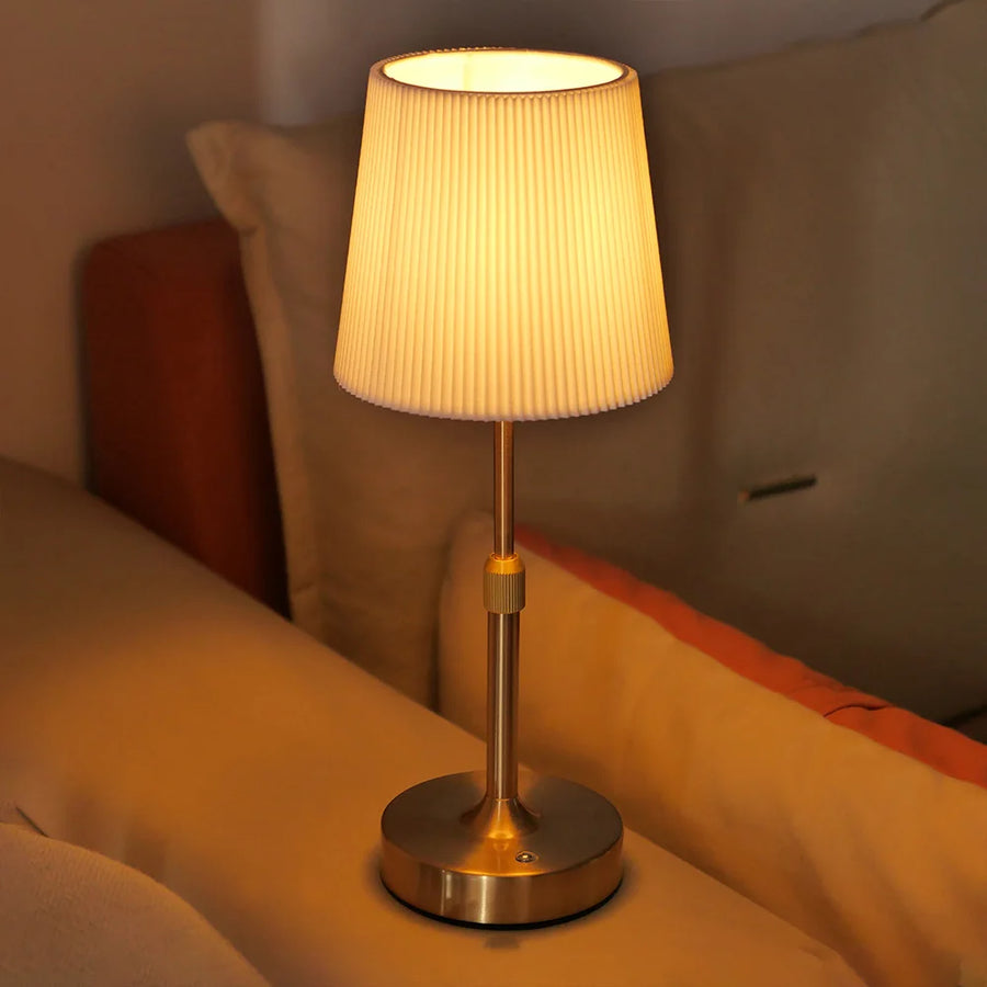 Gold Nella cordless fabric lamp glowing beside a bed