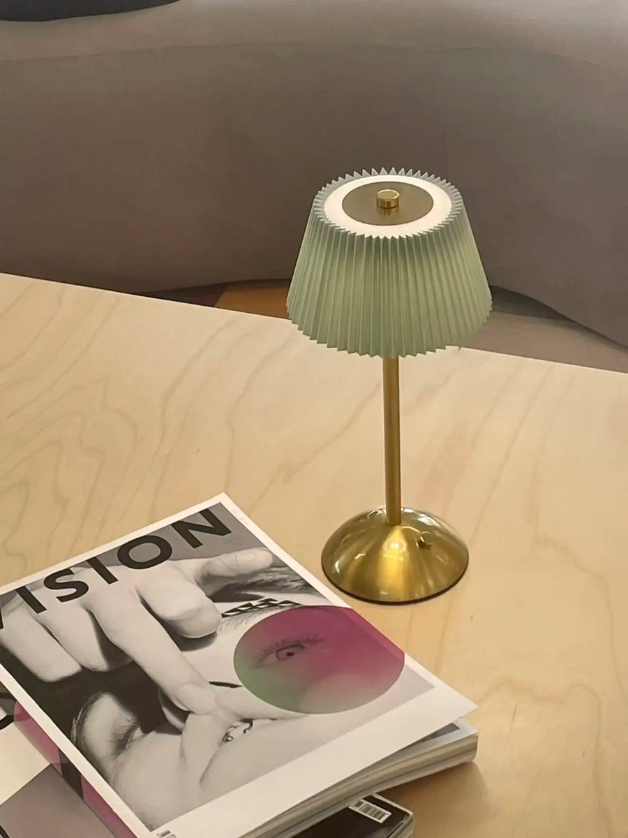 Green Elara pleated lamp beside a magazine on a pale wood table