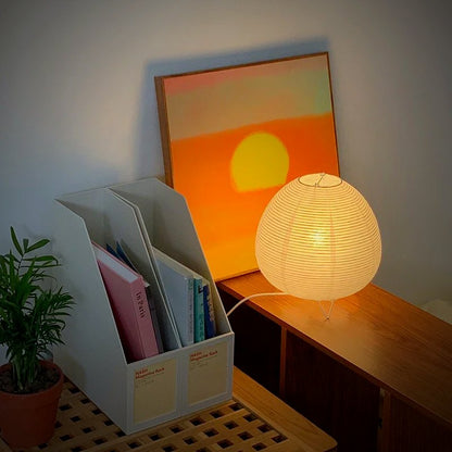 Kana Japanese paper lantern lamp glowing on a shelf beside art prints