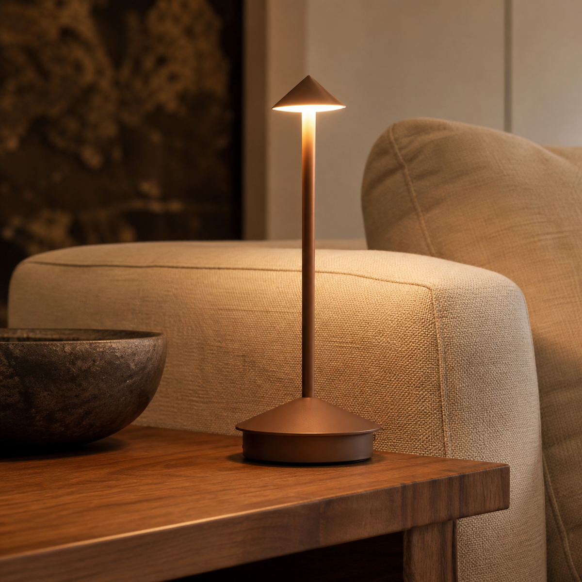 Bronze Sera cordless lamp glowing beside a neutral armchair